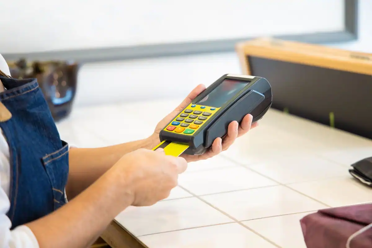 Mâini care folosesc un terminal POS într-un magazin