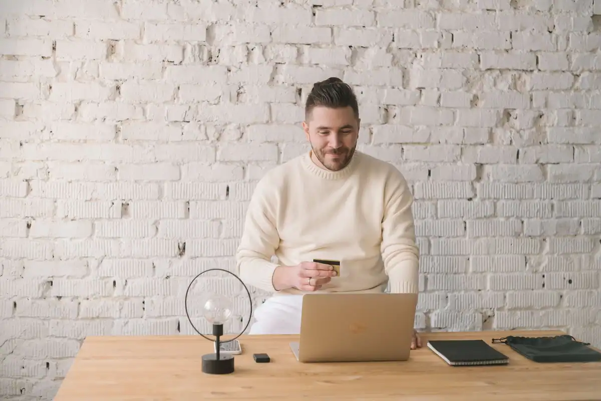 Bărbat care plătește online cu cardul și laptopul, într-un birou luminos și minimalist