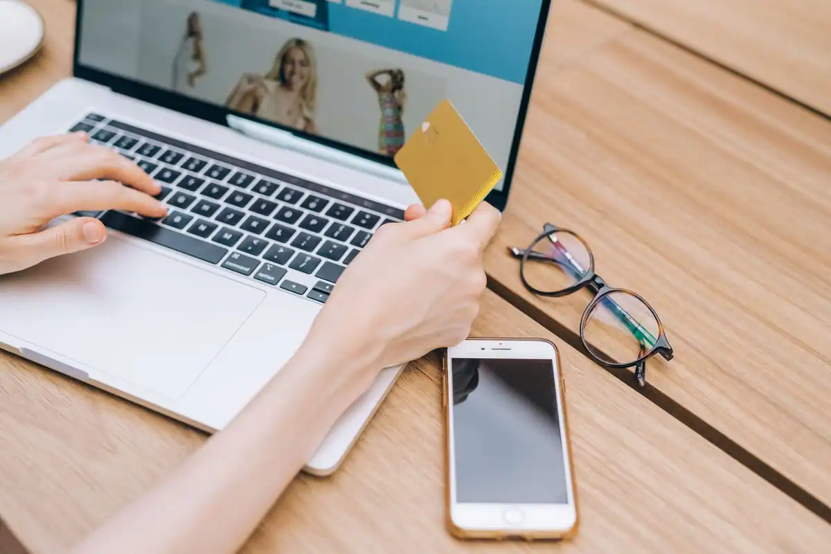 Cumpărătură online făcută cu un card pe laptop, lângă telefon și ochelari