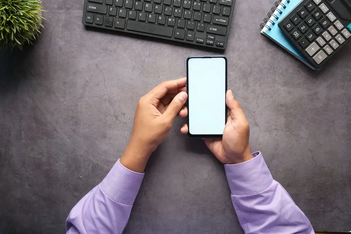Bărbat care ține telefonul la biroul de lucru, lângă tastatură și calculator