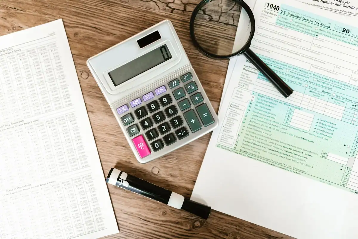 Formulare, calculator și lupă pe o masă de lemn, văzute de sus
