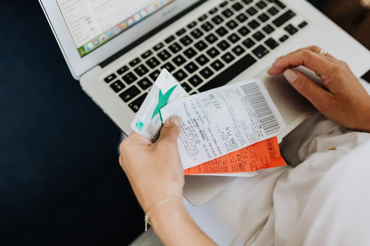 Mâini care țin chitanțe și un card bancar în fața unui laptop