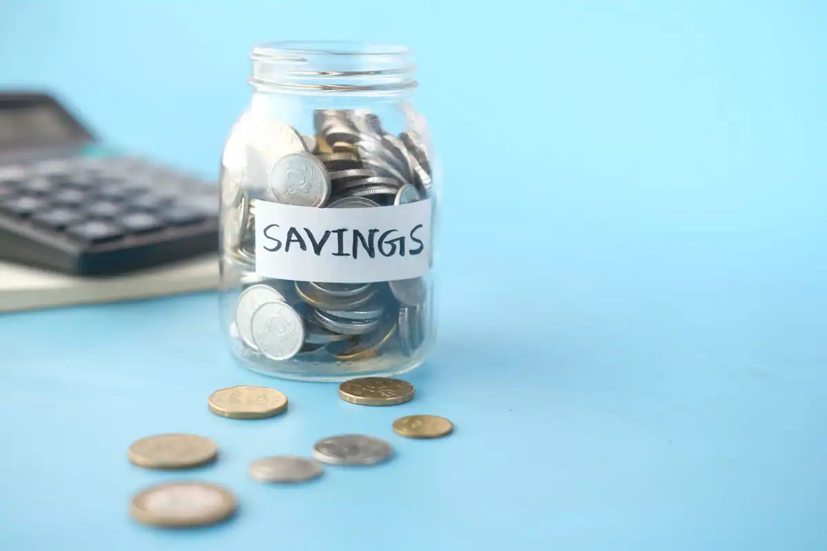 Borcan cu eticheta Savings plin cu monede, lângă un calculator