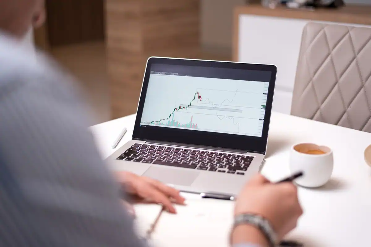 Persoană care analizează date financiare pe laptop, cu o cafea alături