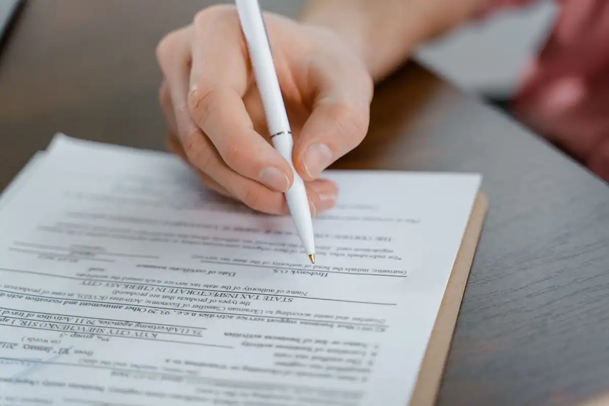 Mână cu pix care semnează un document, cu hârtia în prim-plan