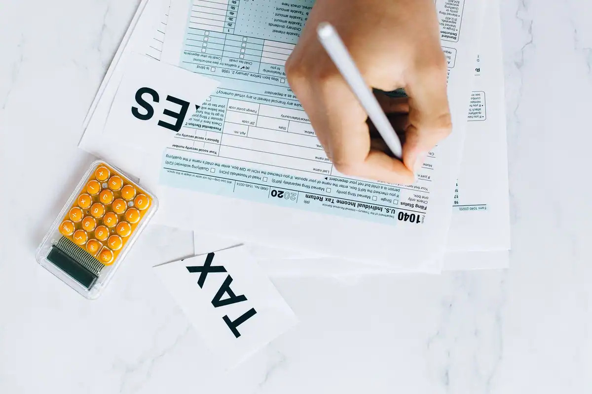 Mână care completează un formular, cu un calculator alături