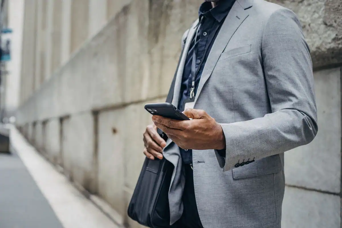 Bărbat la costum care își citește mesajele pe telefon pe stradă