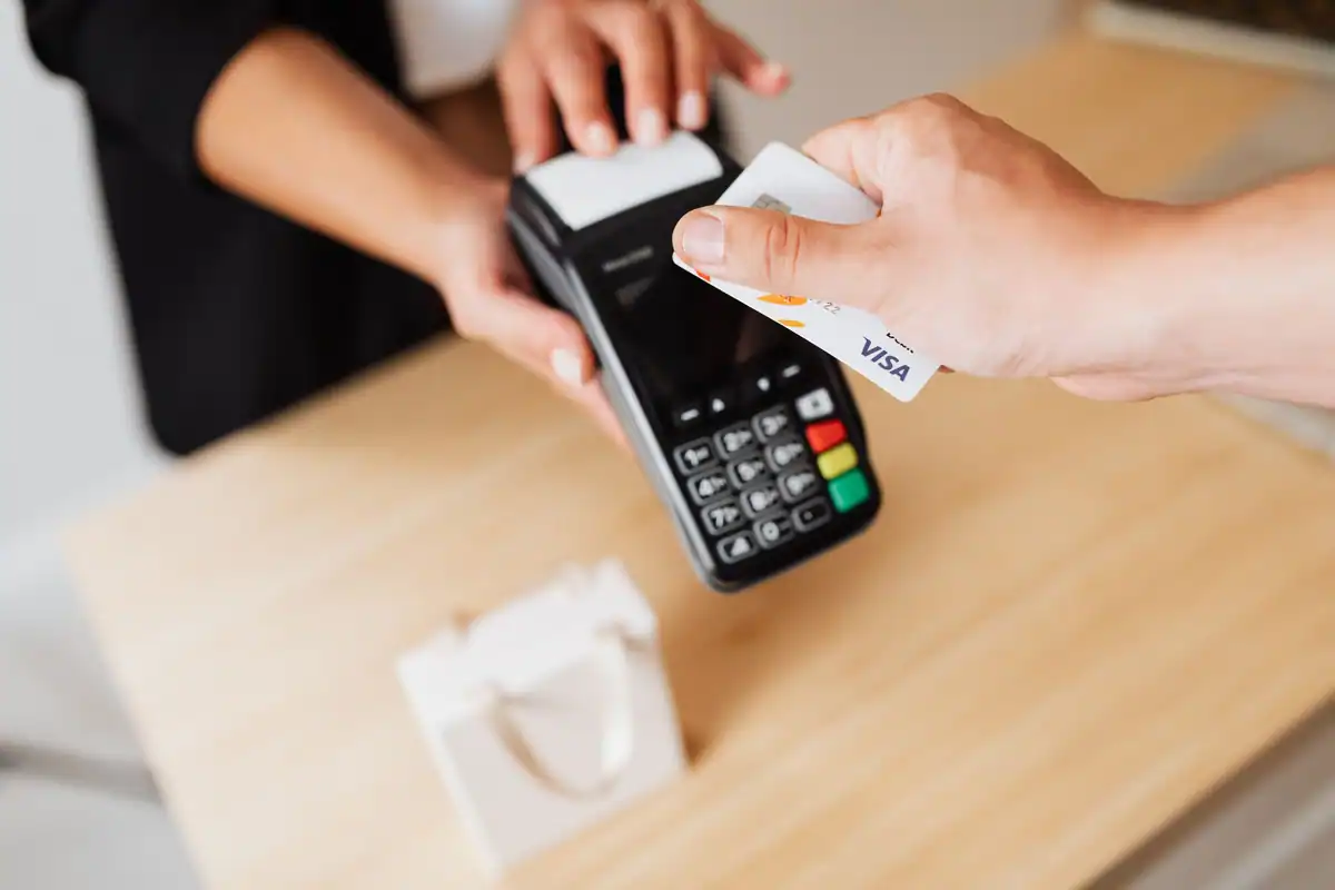 Mâini care apropie un card de un terminal contactless