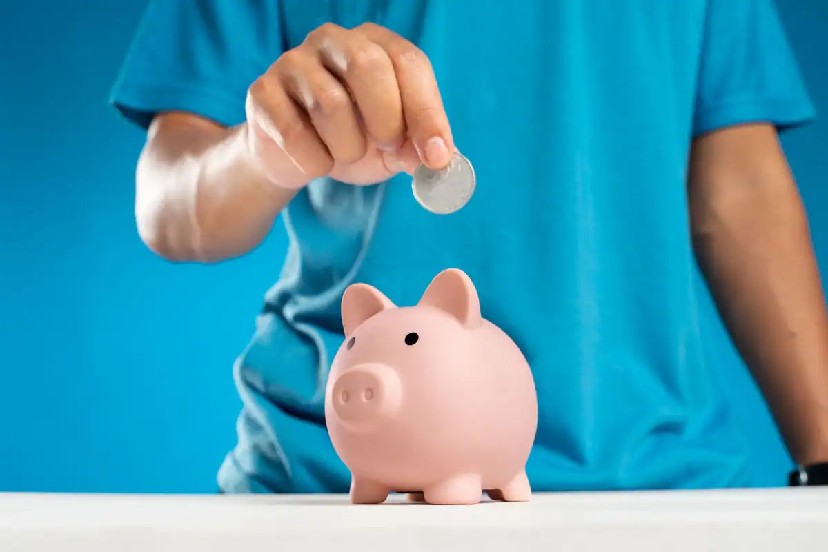 Mână care pune o monedă într-o pușculiță, economisire pe termen lung