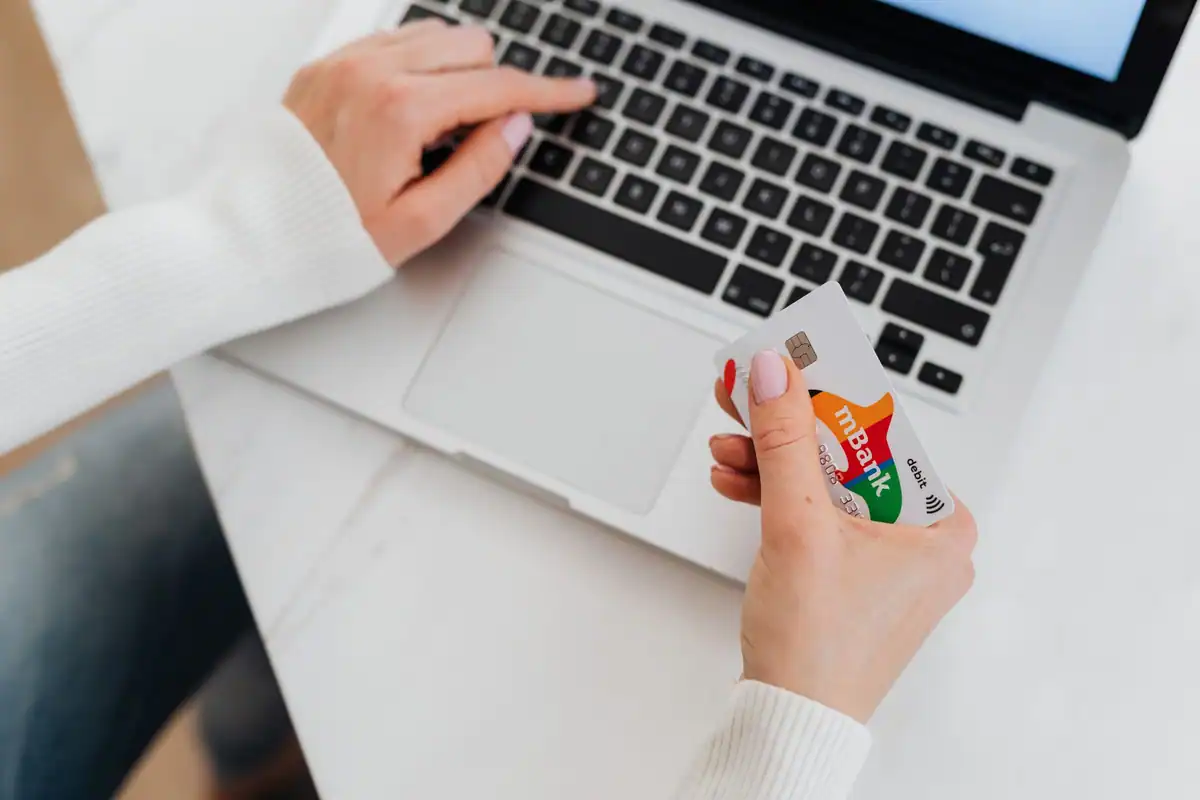 Persoană care ține un card bancar în timp ce folosește laptopul