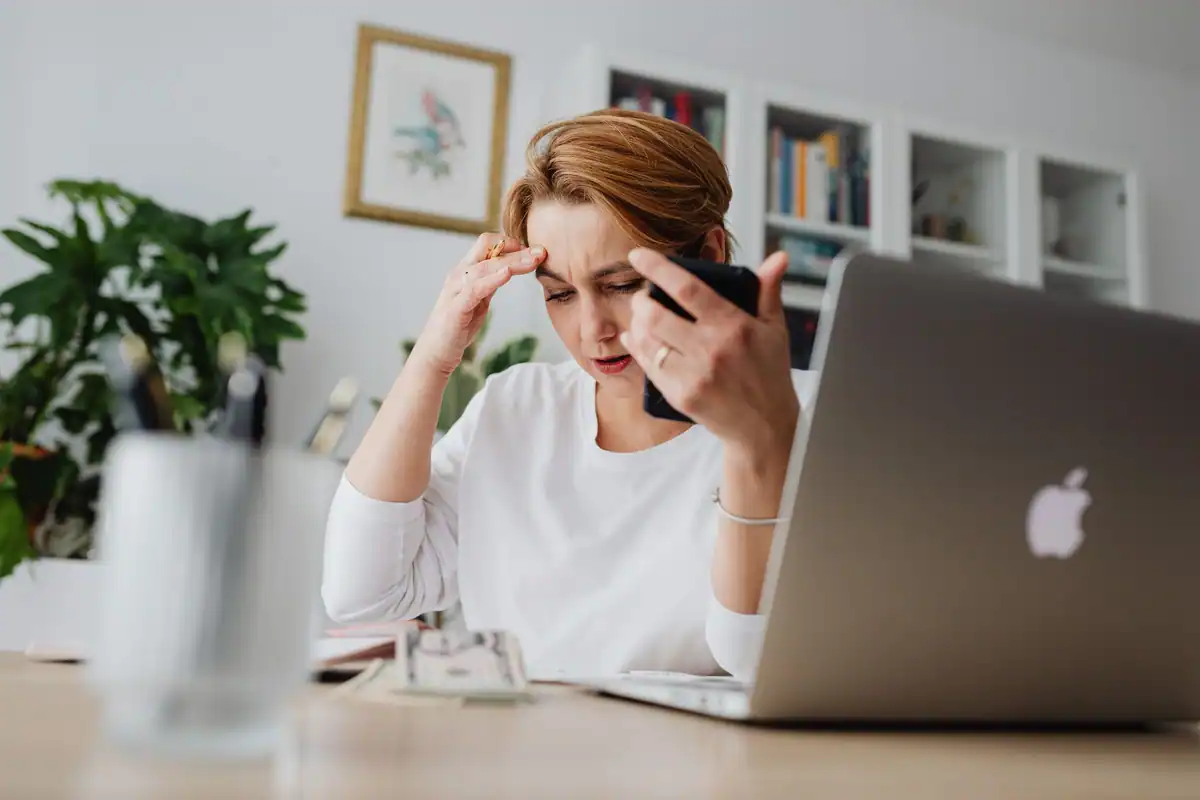 Femeie stresată cu telefonul în mână, la birou, după o plată greșită